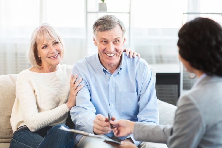 Insurance Concept. Happy senior couple consulting with female agent at home, signing papers